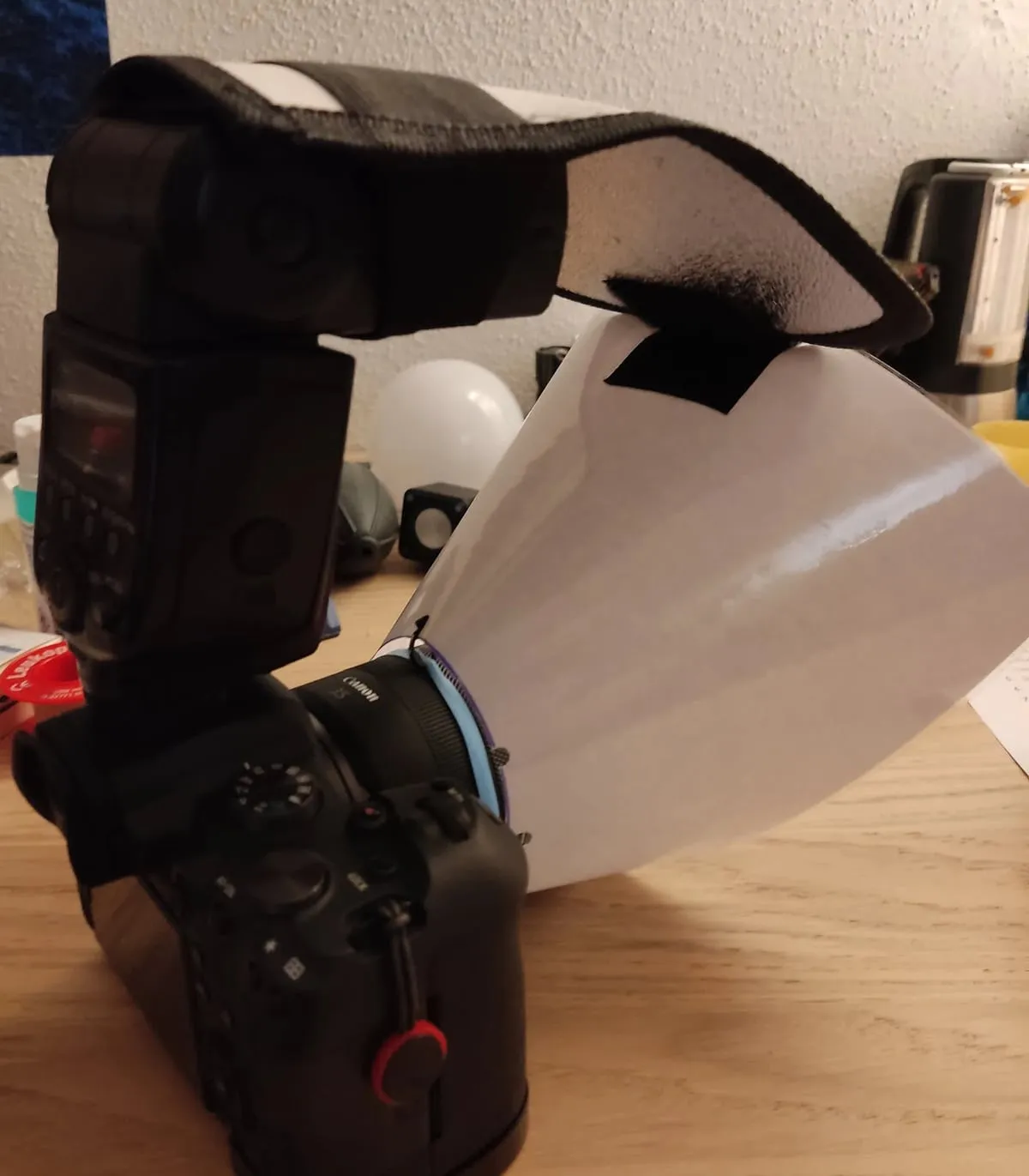 Canon-Kamera mit Aufsteckblitz. Ein biegsamer Reflektor am Blitzkopf lenkt das Licht in einen Trichter aus weißer Kunststofffolie, der vorn um das Objektiv sitzt.