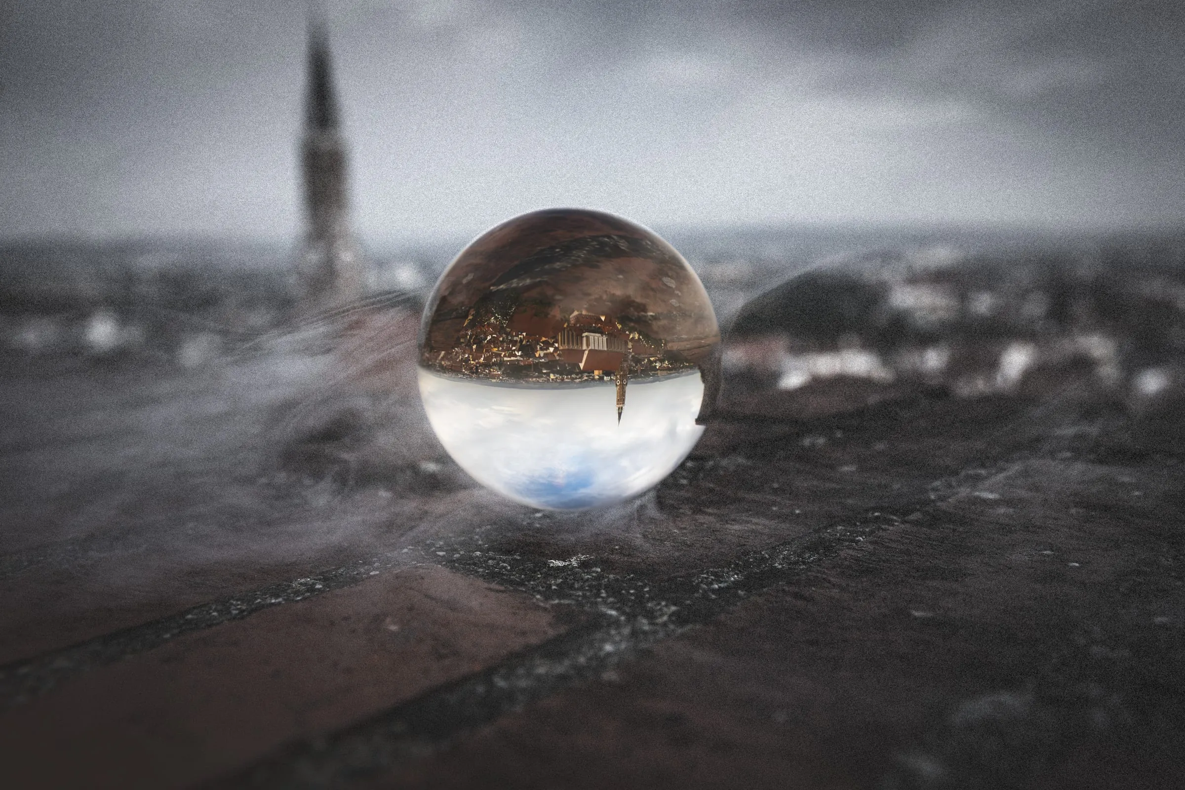 Glass ball on an old brick wall showing the old town and St. Martin’s tower upside down, with the same tower blurred behind it under a grey sky.